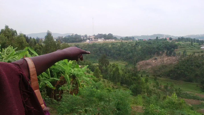 Aha Mukankusi arerekana aho ubutaka bwe buhingwaho buherera mu mubande.