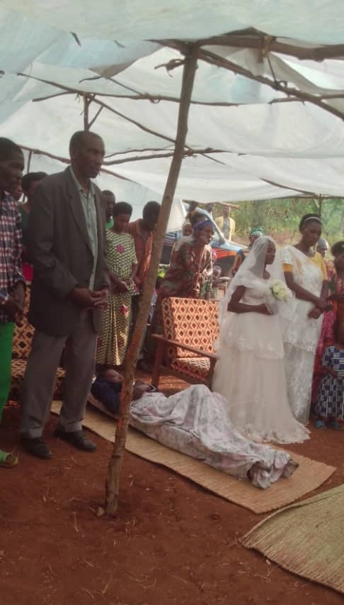 Bizumuremyi Jean uryamye hagati y'uwamuherekeje (Parrain) n'umugore we, yahawe amasakaramentu, arasezerana, aranabatirisha